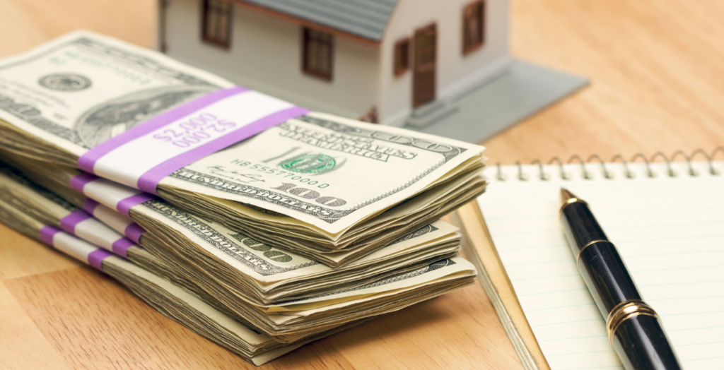 cash next to a note pad and a model of a home