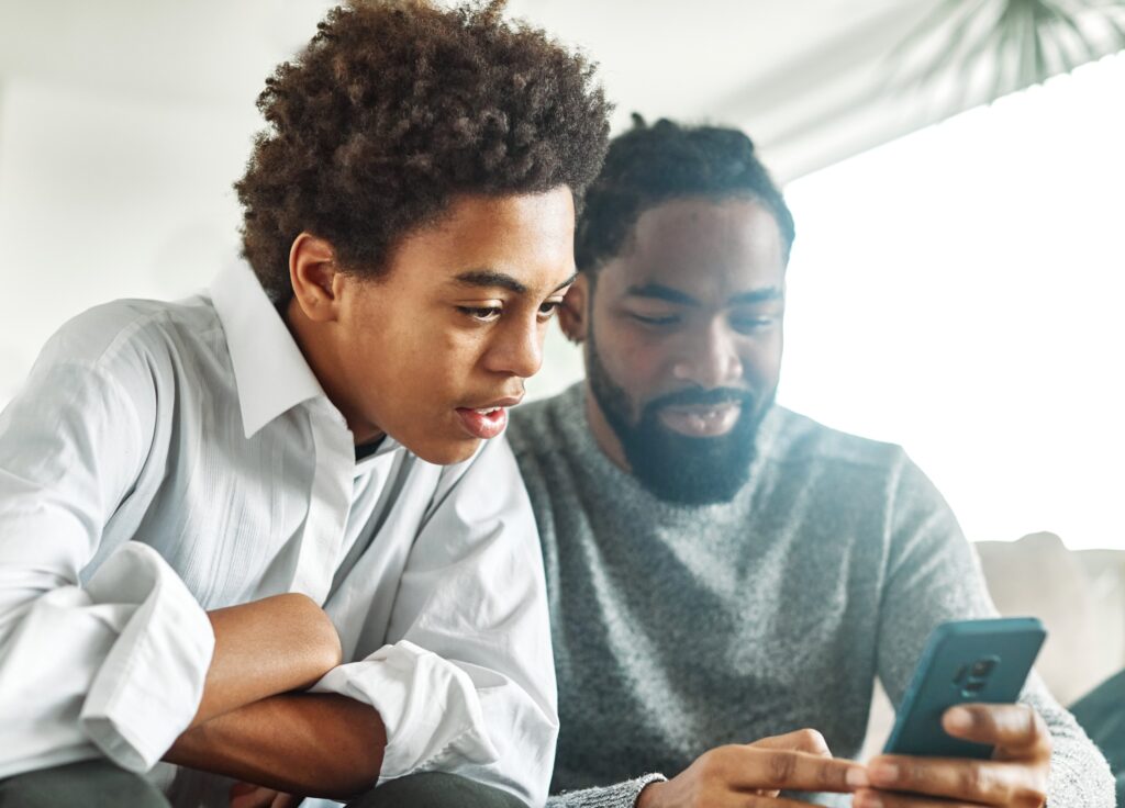 Father and son looking at cell phone talking about financial journey